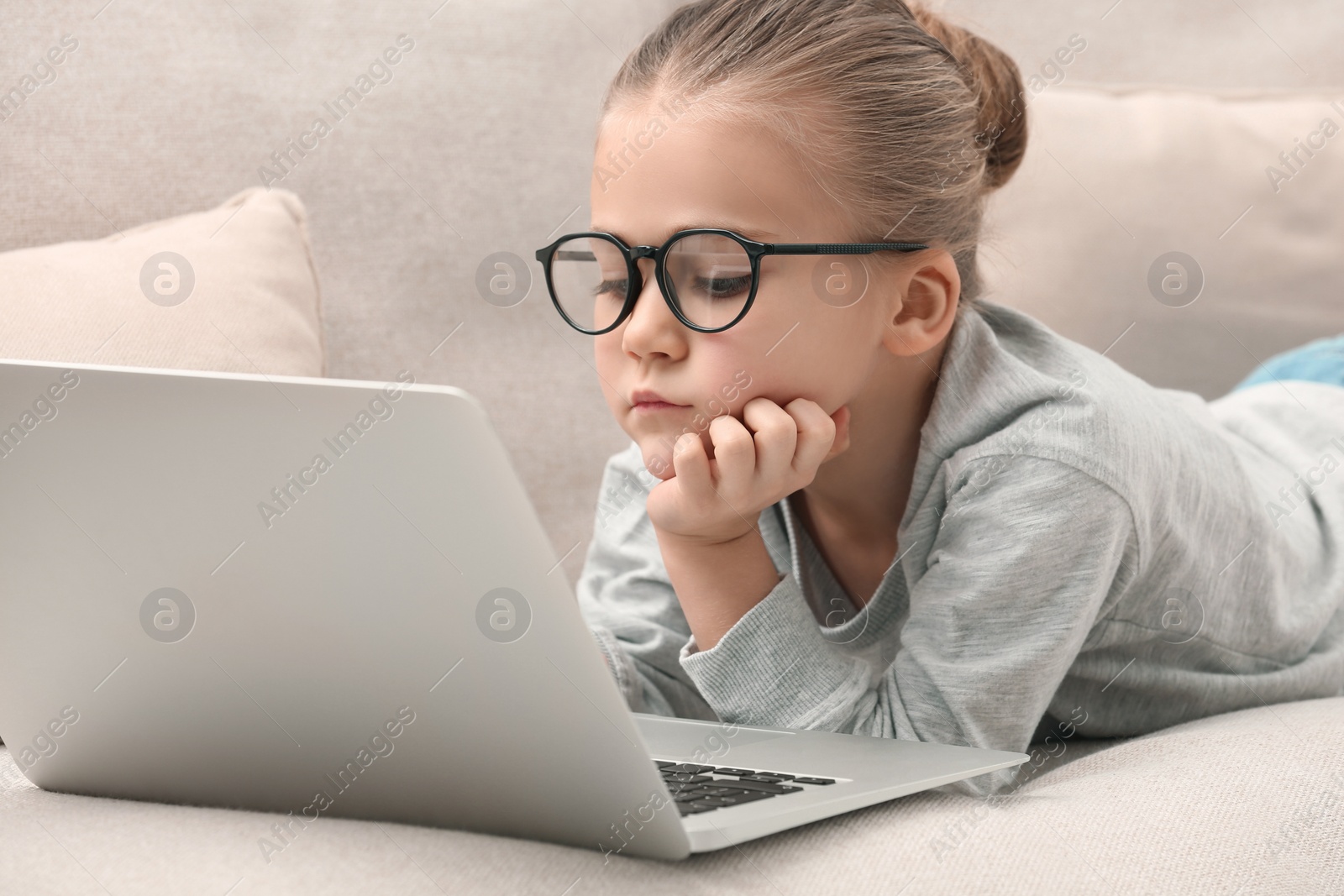 Photo of Little girl in glasses with laptop on sofa