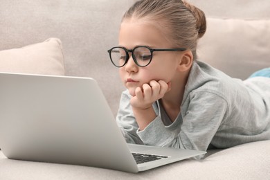 Little girl in glasses with laptop on sofa