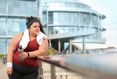 Beautiful overweight woman in sportswear with bottle and towel outdoors
