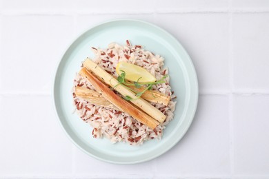 Plate with baked salsify roots, lemon and rice on white tiled table, top view