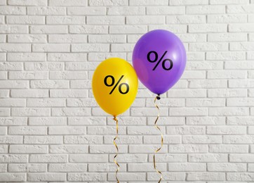 Image of Discount offer. Purple and yellow balloons with percent sign against white brick wall