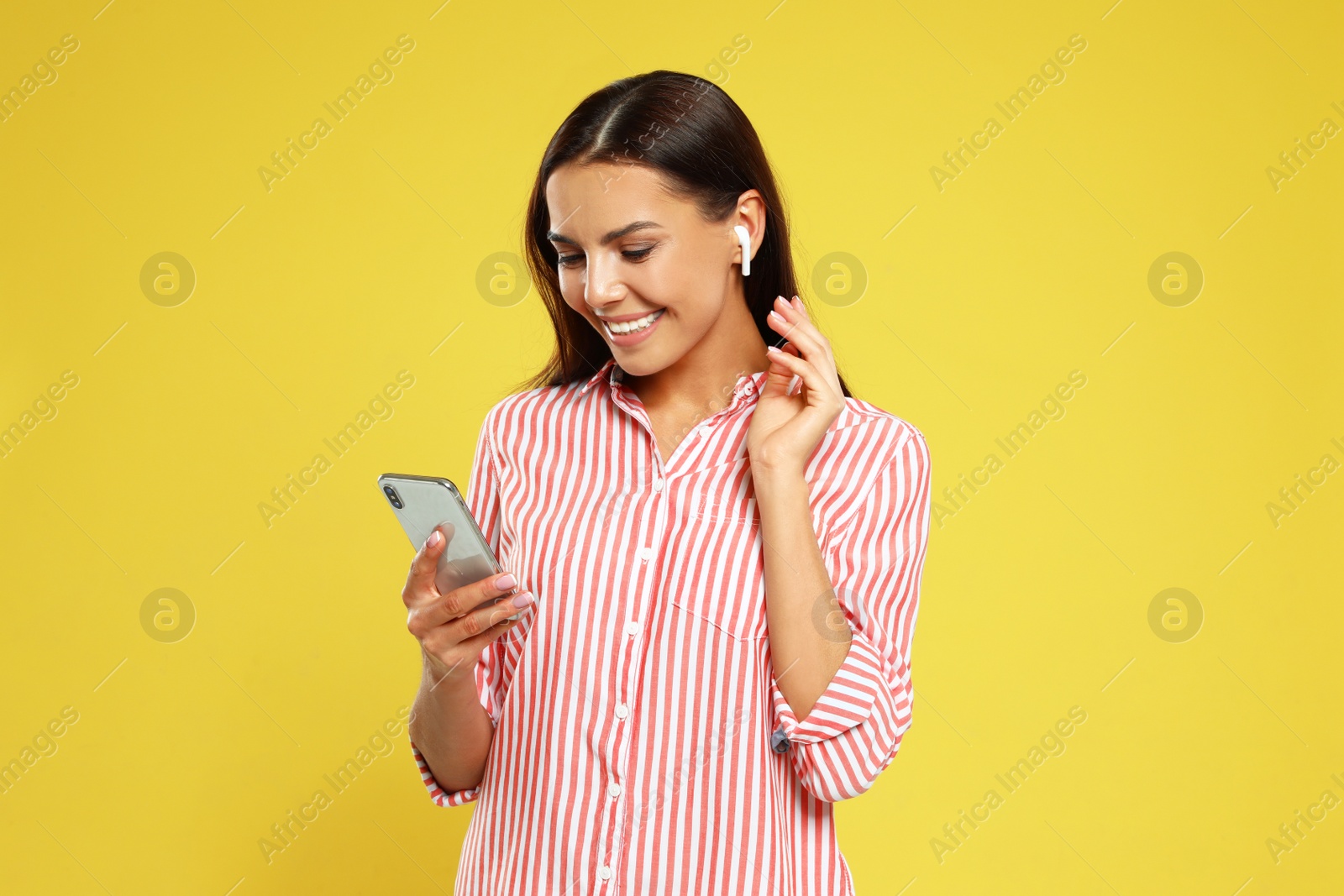 Photo of Happy young woman with smartphone listening to music through wireless earphones on yellow background