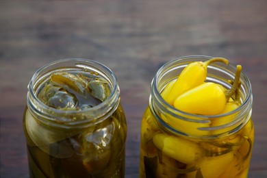 Glass jars of pickled green and yellow jalapeno peppers on wooden table, closeup