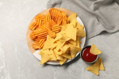 Photo of Tasty ketchup with ridged and tortilla chips on grey table, flat lay