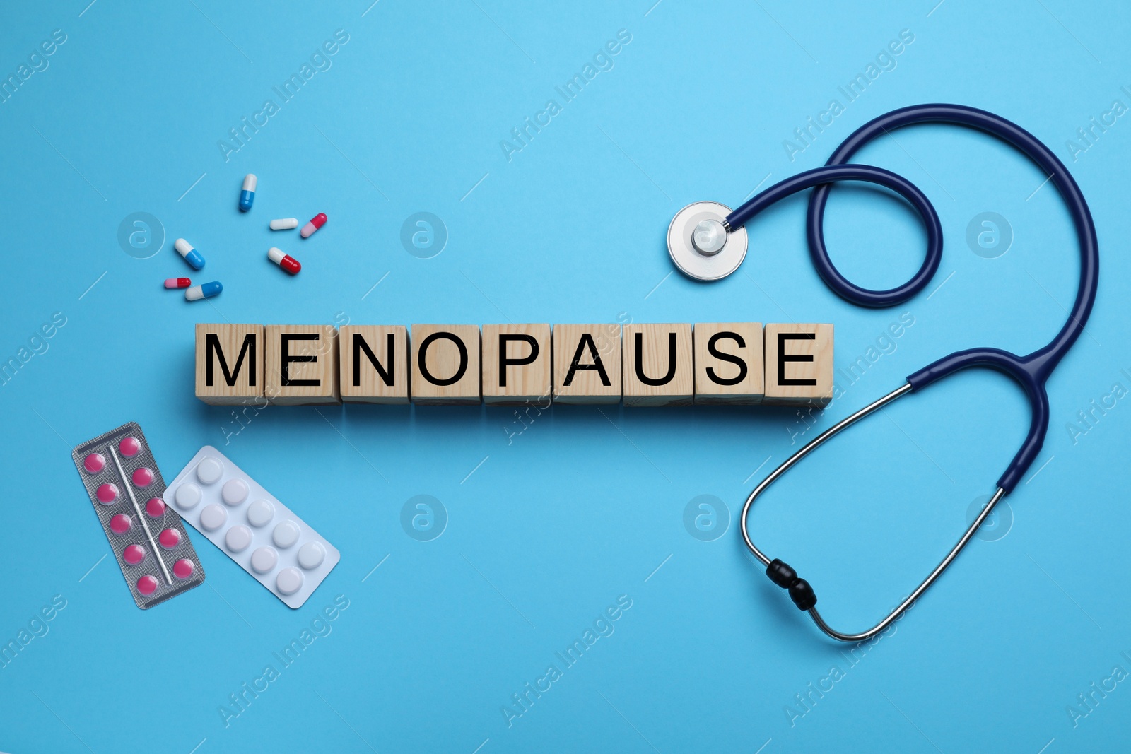 Photo of Wooden cubes with word Menopause, stethoscope and pills on light blue background, flat lay