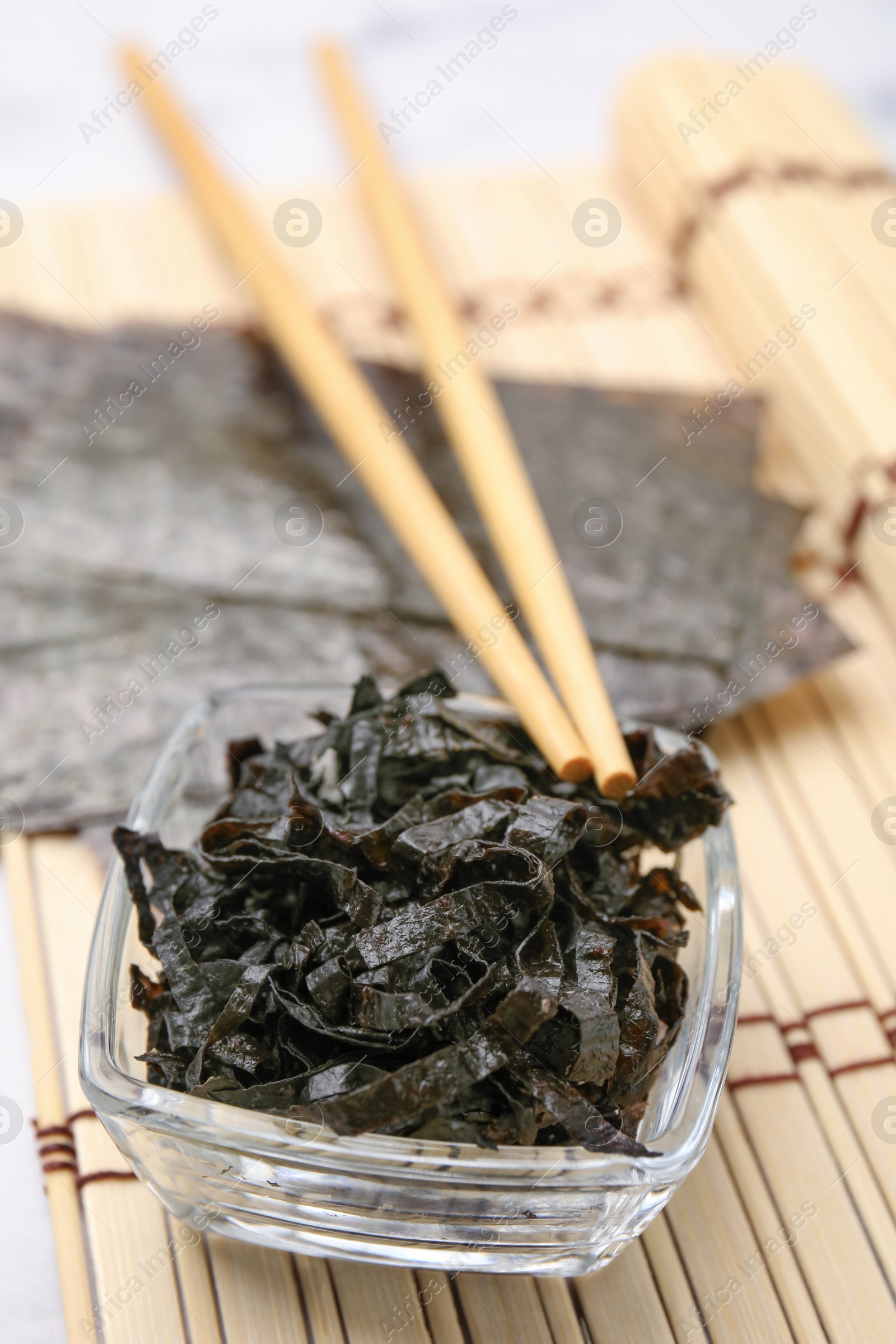 Photo of Chopped nori sheets with chopsticks on bamboo mat, closeup