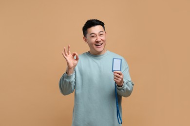 Happy asian man with vip pass badge showing ok gesture on beige background
