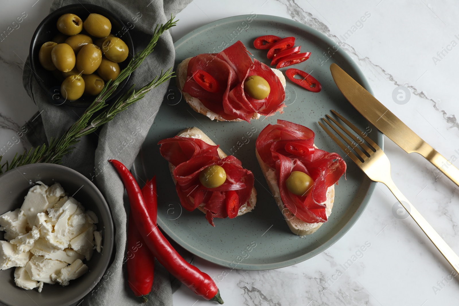 Photo of Delicious sandwiches with bresaola, cream cheese and olives served on white marble table, flat lay