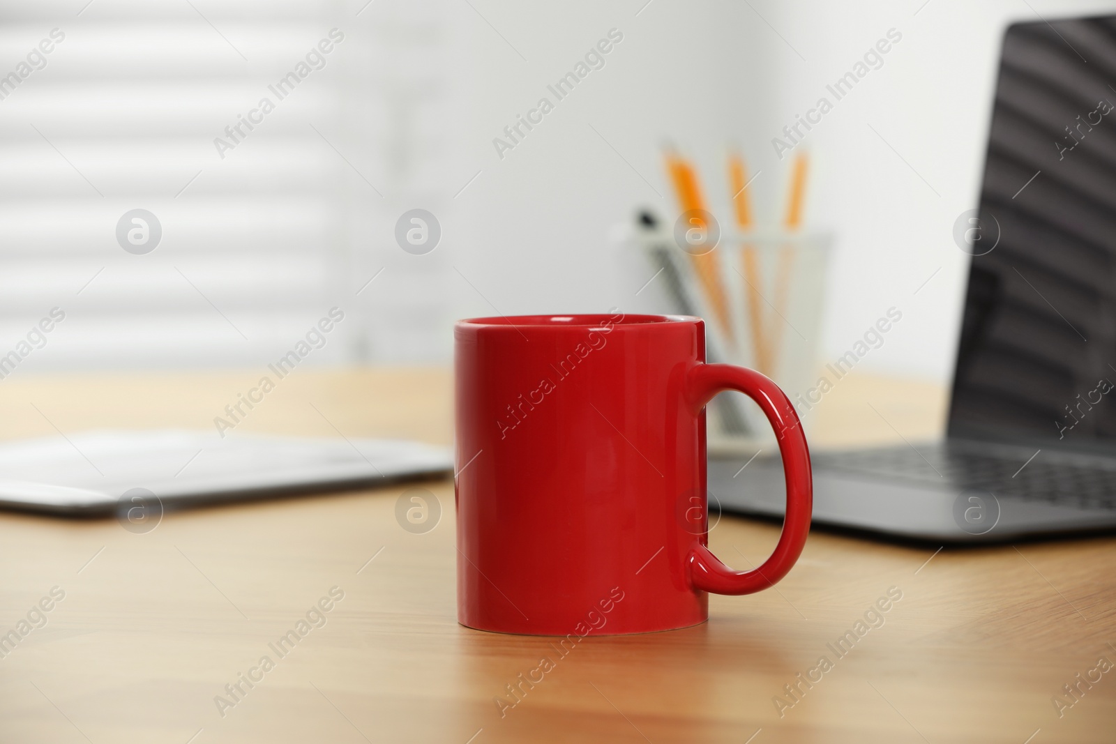 Photo of Red ceramic mug on wooden table at workplace. Mockup for design