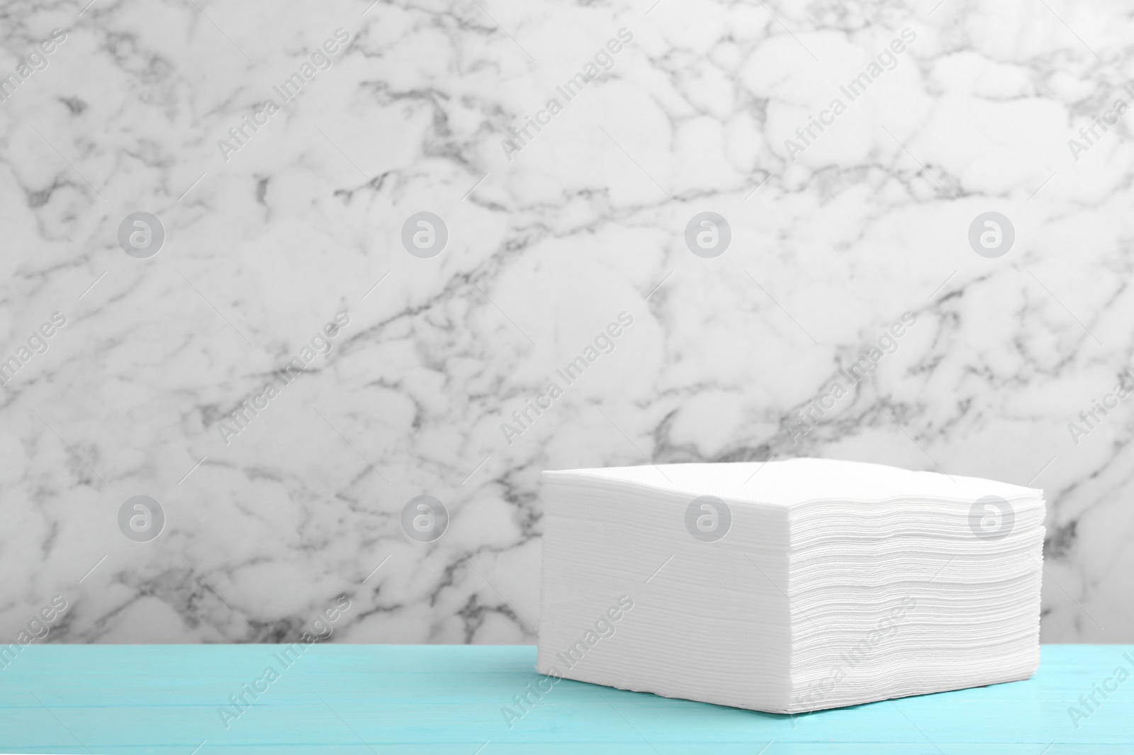 Photo of Stack of napkins on turquoise wooden table against marble wall, space for text