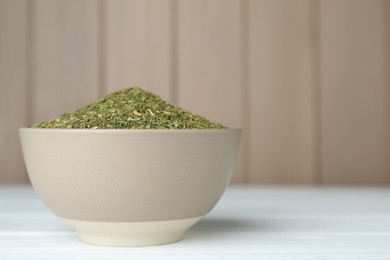 Photo of Dried dill in bowl on white wooden table, space for text