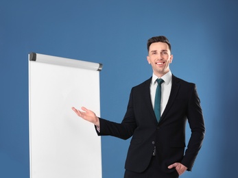 Young business trainer near flip chart on color background