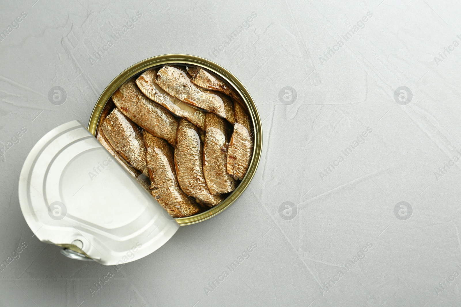 Photo of Open tin can of sprats on light grey table, top view. Space for text