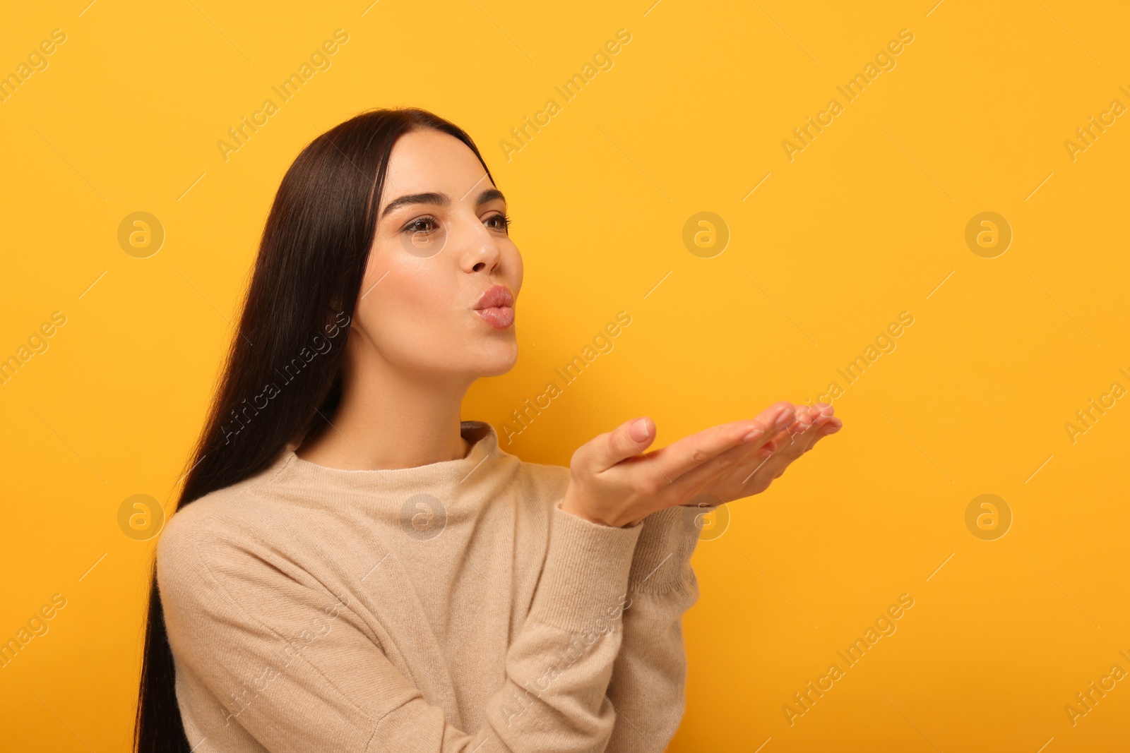 Photo of Beautiful young woman blowing kiss on orange background. Space for text