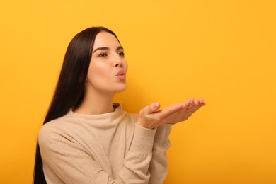 Beautiful young woman blowing kiss on orange background. Space for text