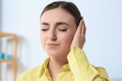 Young woman suffering from ear pain indoors