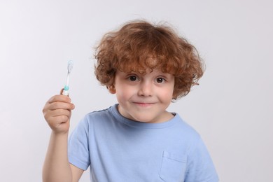 Photo of Cute little boy holding plastic toothbrush on white background