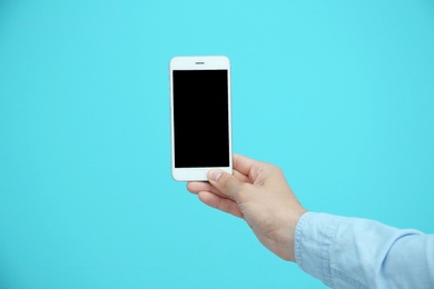 Photo of Young man holding mobile phone with blank screen in hand on color background
