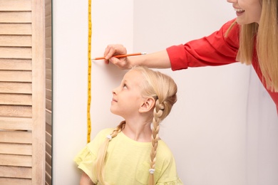 Photo of Young woman measuring her daughter's height at home