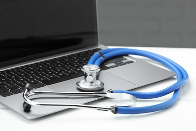 Photo of Stethoscope and modern laptop on white table