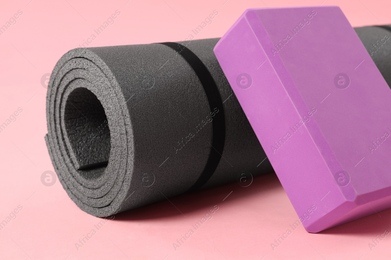Photo of Grey exercise mat and yoga block on pink background, closeup