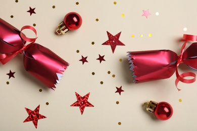 Photo of Open red Christmas cracker and decorations with shiny confetti on beige background, flat lay