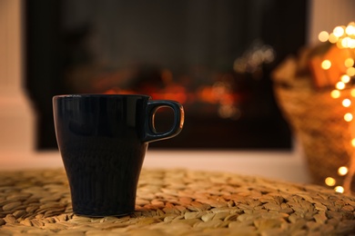 Photo of Dark blue cup with hot drink against fireplace, space for text