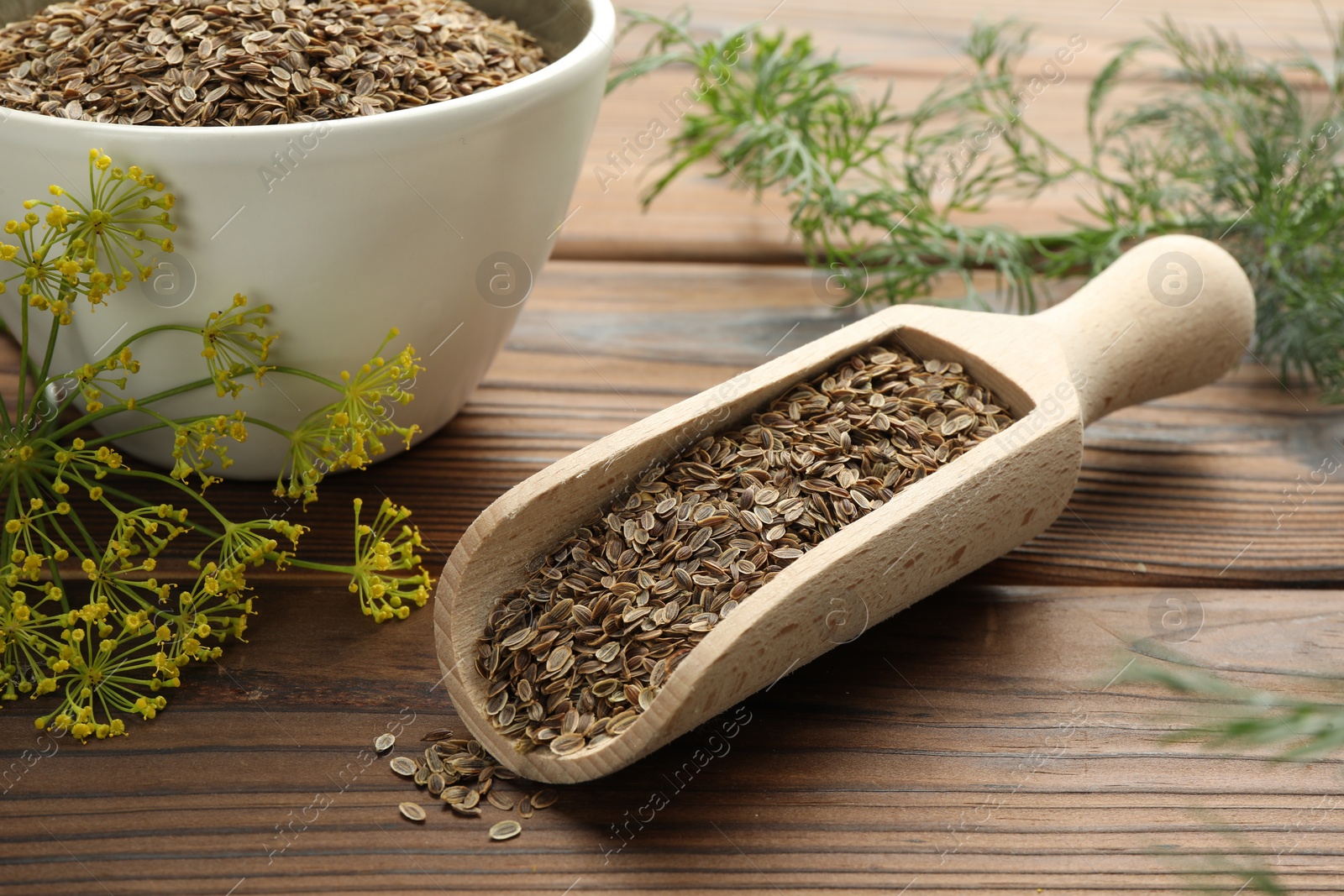 Photo of Scoop of dry seeds, bowl and fresh dill on wooden table, closeup