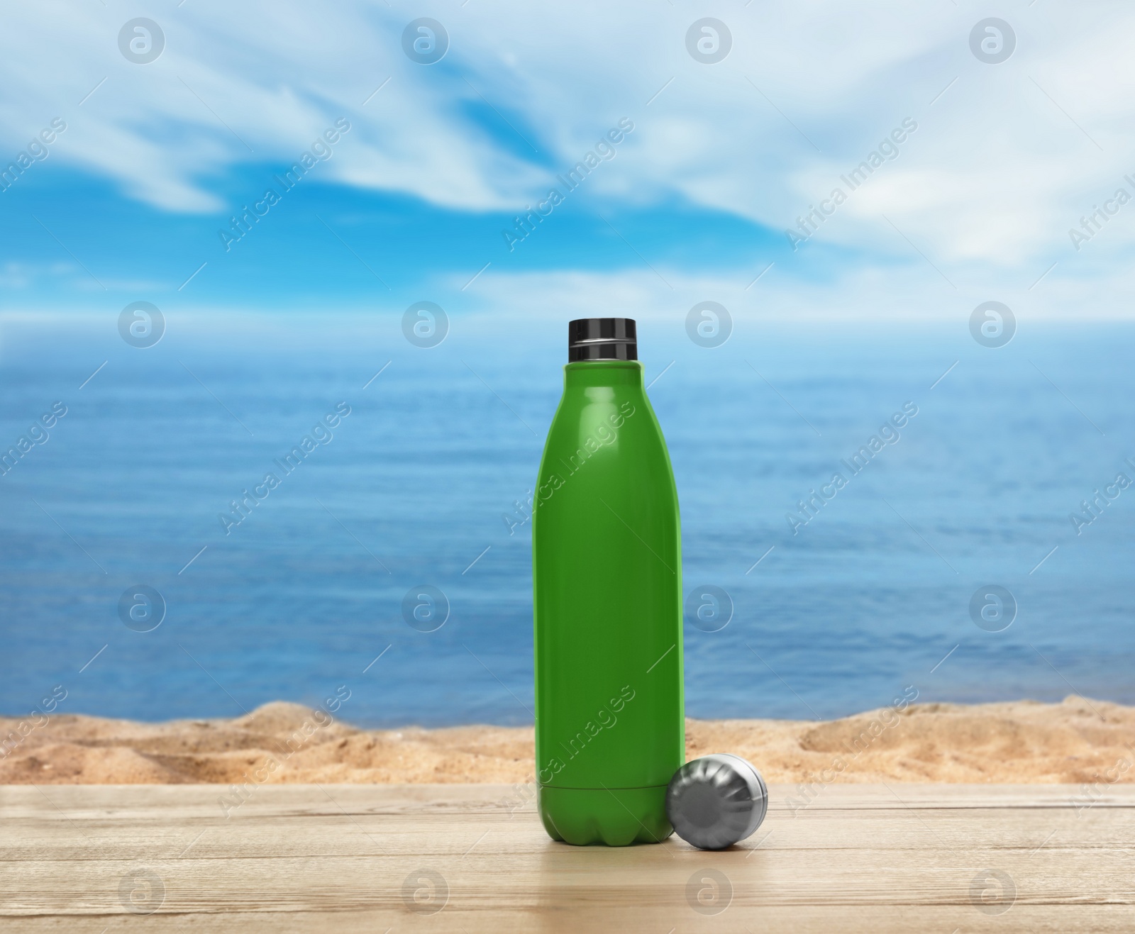 Image of Thermo bottle on wooden table near sea under blue sky