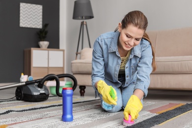 Photo of Young woman cleaning carpet at home