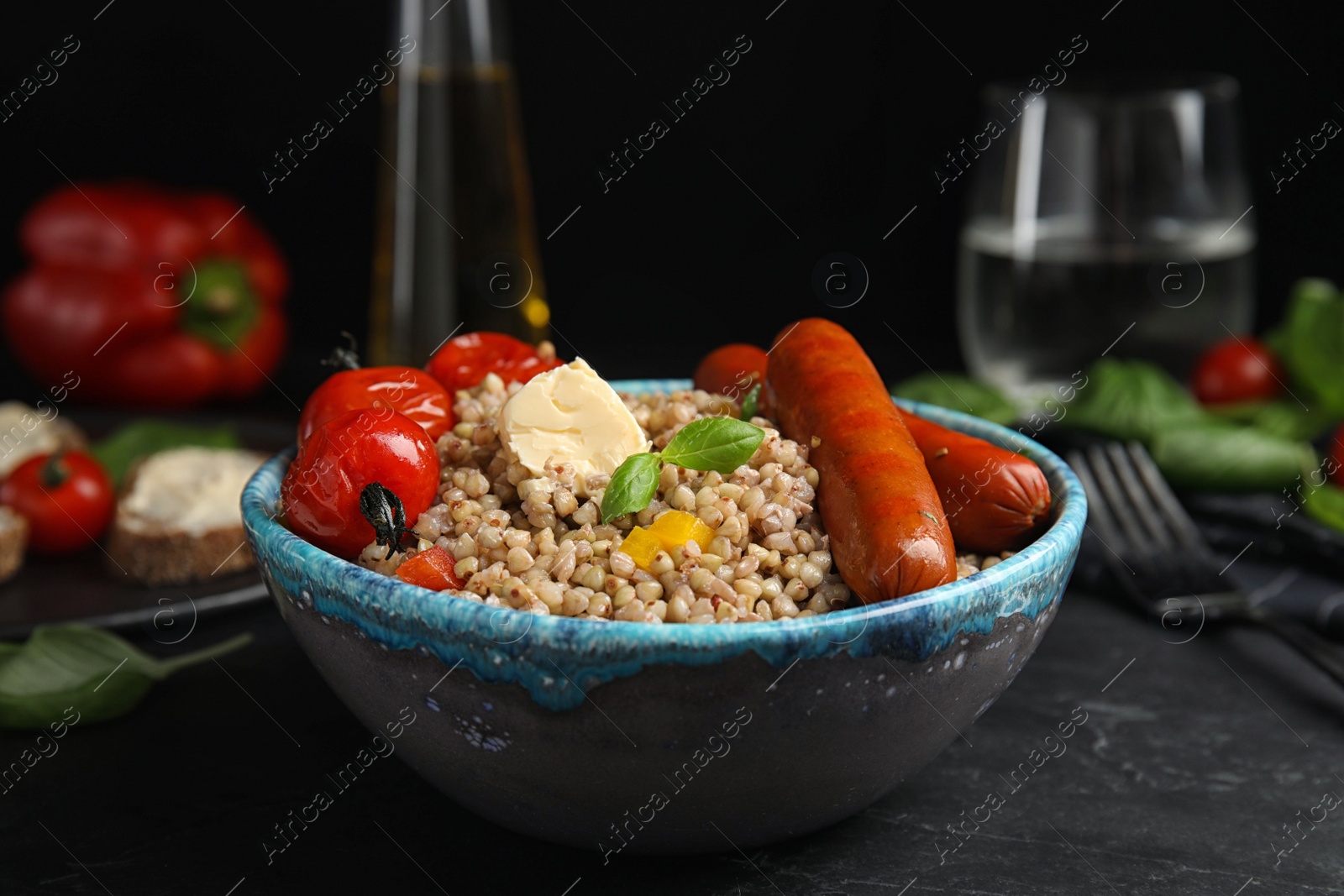 Photo of Tasty buckwheat porridge with sausages on black table