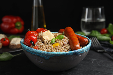 Tasty buckwheat porridge with sausages on black table