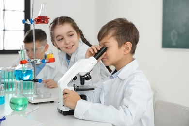 Schoolboy looking through microscope and his classmates at chemistry lesson