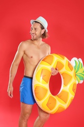 Photo of Attractive young man in beachwear with pineapple inflatable ring on red background