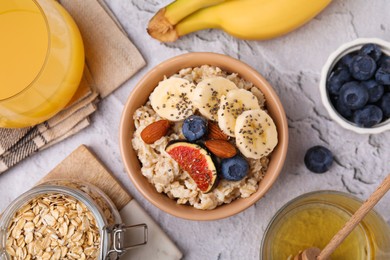 Bowl of oatmeal with blueberries, almonds, banana and fig pieces on white textured table, flat lay