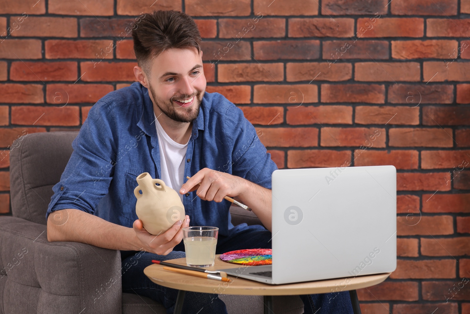 Photo of Happy man showing clay vase on online course by videochat at home. Time for hobby