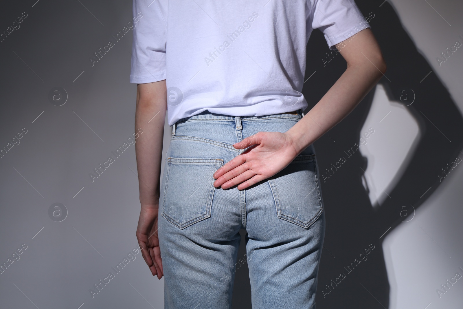 Photo of Woman showing open palm behind her back on grey background, back view