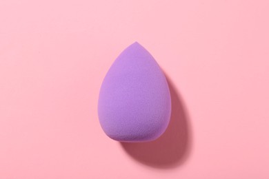 Photo of Purple makeup sponge on pink background, top view