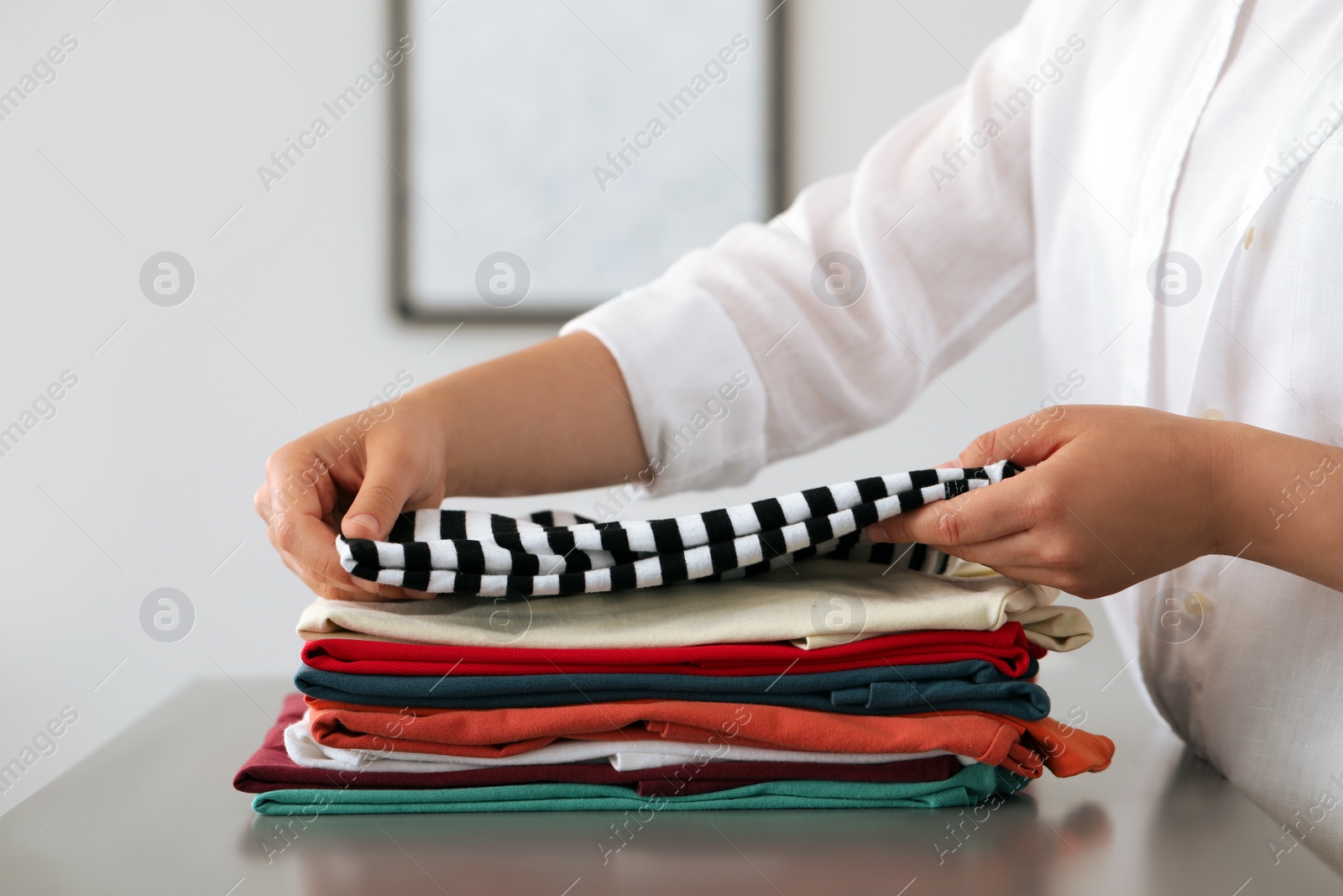 Photo of Woman folding clothes at grey table indoors, closeup