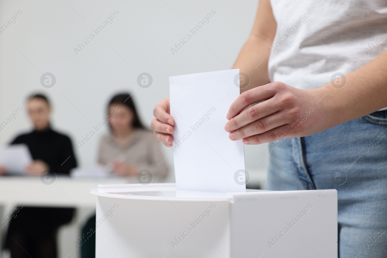 Photo of Woman putting her vote into ballot box on blurred background, closeup