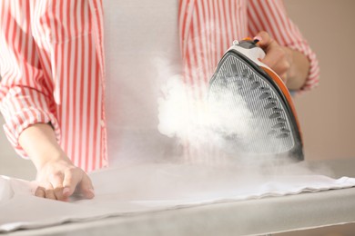 Image of Woman ironing clean laundry with steam, closeup