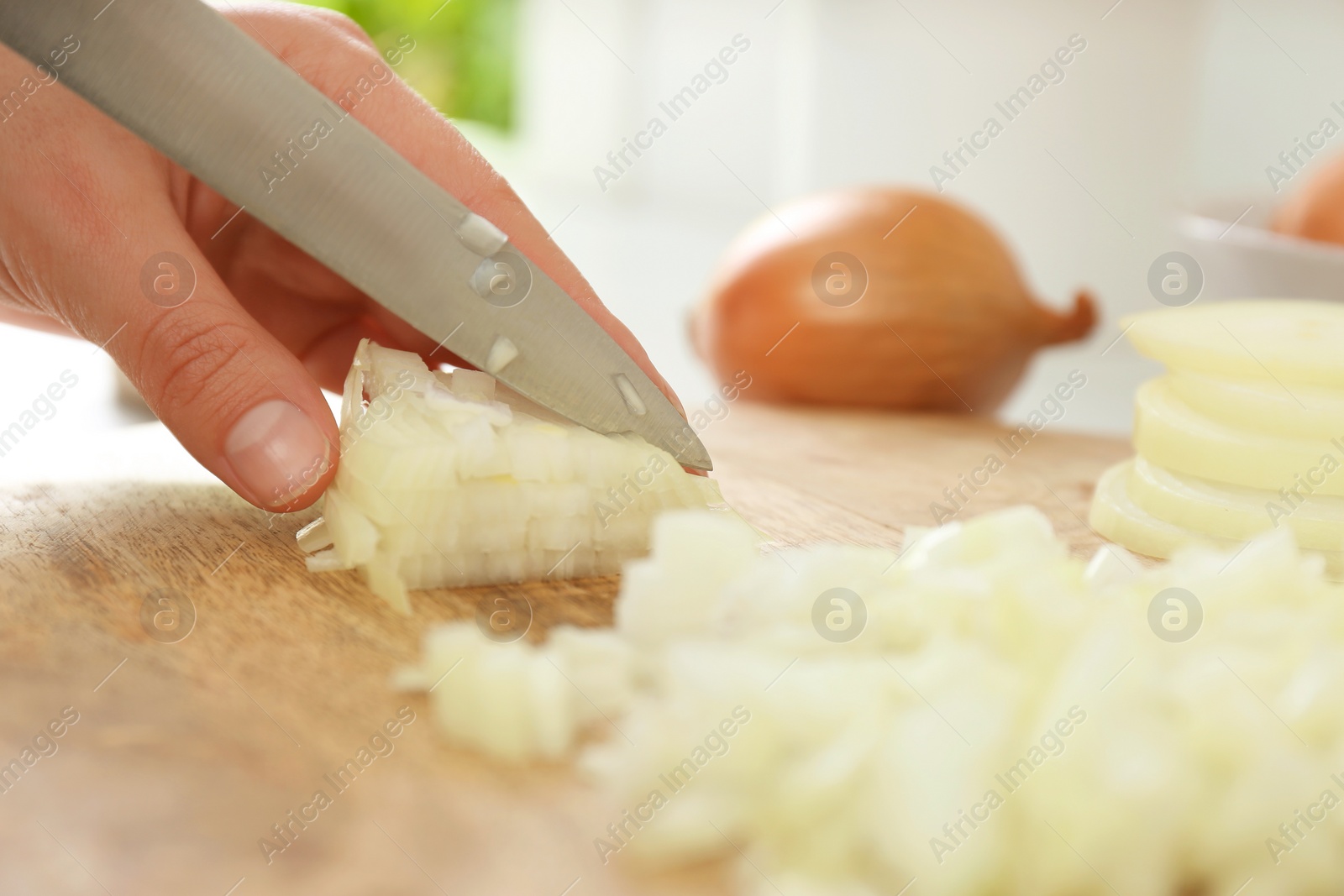 Photo of Woman chopping white onion on wooden board at table, closeup