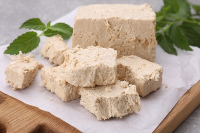 Pieces of tasty halva and mint leaves on table, closeup