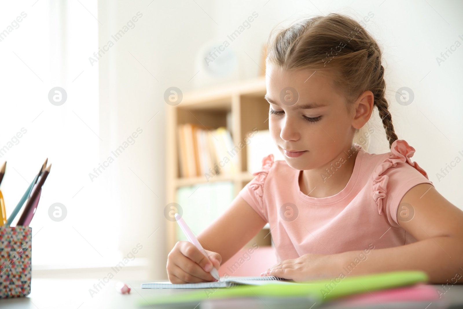 Photo of Cute little child doing assignment at desk in classroom. Elementary school