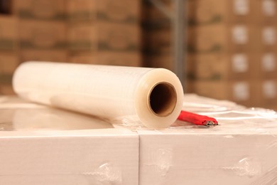 Photo of Roll of stretch film and utility knife on wrapped boxes in warehouse