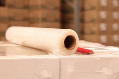 Roll of stretch film and utility knife on wrapped boxes in warehouse