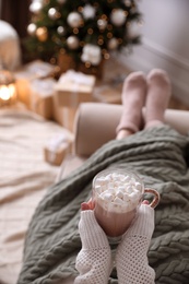 Photo of Woman with delicious hot drink wrapped in plaid on sofa at home, closeup