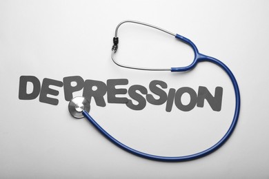 Photo of Word Depression and stethoscope on white background, flat lay
