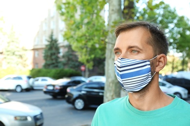 Photo of Man wearing handmade cloth mask outdoors, space for text. Personal protective equipment during COVID-19 pandemic