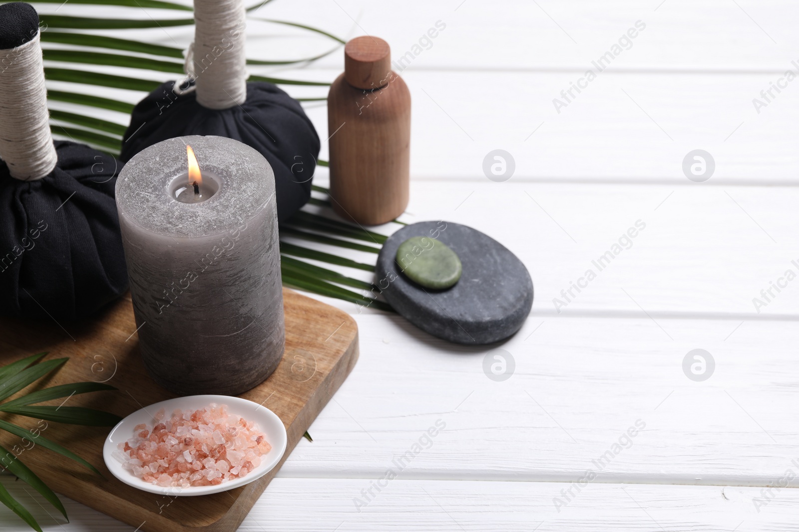 Photo of Beautiful spa composition with herbal massage bags, burning candle and leaves on white wooden table. Space for text